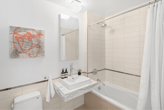 bathroom featuring tile walls, toilet, tiled shower / bath, and a sink