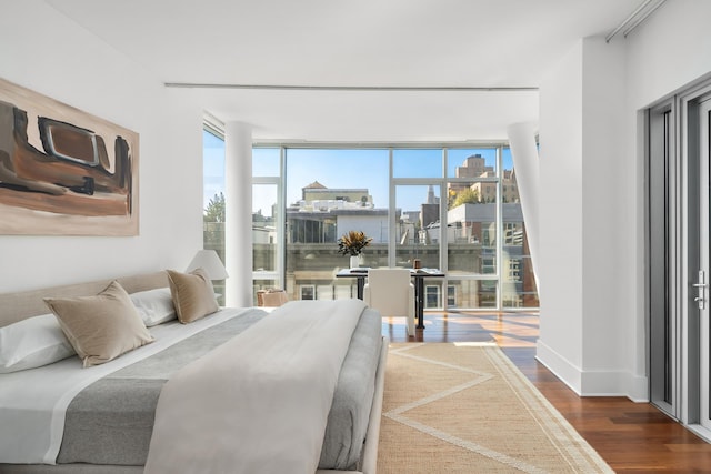 bedroom featuring a view of city, a wall of windows, baseboards, and wood finished floors