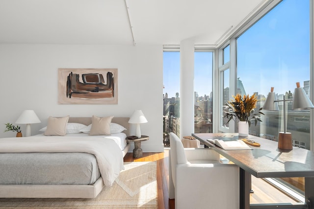 bedroom with a city view, a wall of windows, and wood finished floors