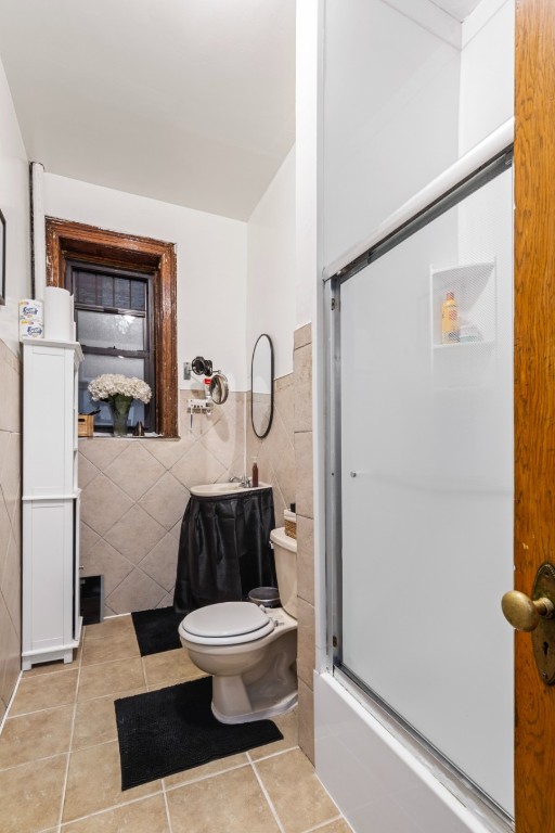 bathroom featuring enclosed tub / shower combo, tile patterned floors, toilet, and tile walls