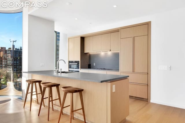 kitchen featuring sink, oven, kitchen peninsula, light brown cabinets, and light hardwood / wood-style flooring