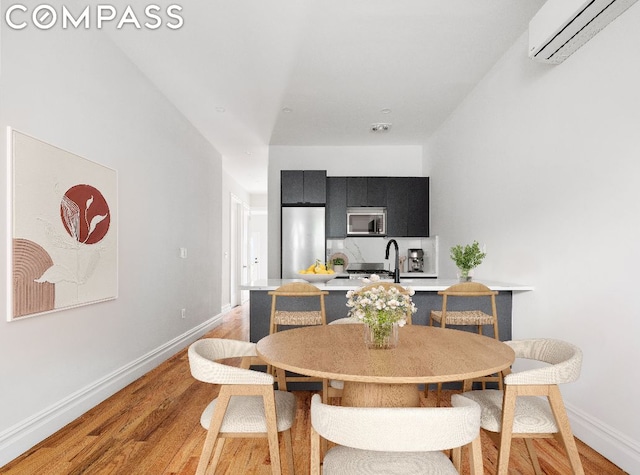 dining room with sink, a wall mounted AC, and light hardwood / wood-style floors