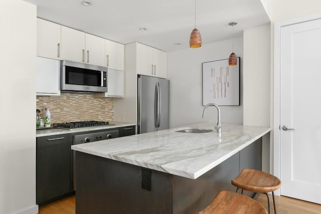 kitchen with a breakfast bar area, stainless steel appliances, pendant lighting, white cabinets, and sink