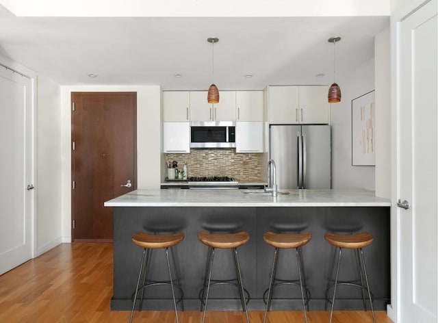 kitchen with white cabinetry, stainless steel appliances, backsplash, hanging light fixtures, and sink