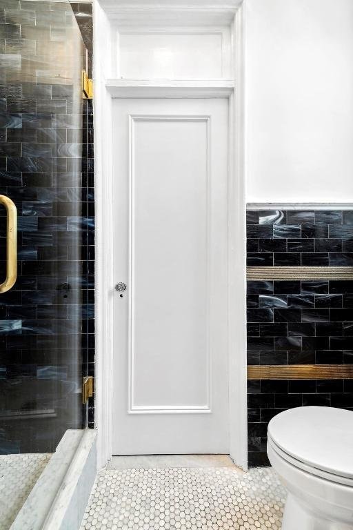 bathroom featuring tile walls, toilet, an enclosed shower, and tile patterned flooring