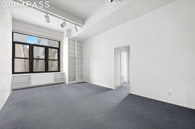 empty room with dark carpet, built in shelves, and a textured ceiling