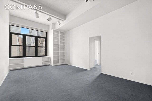 unfurnished room with a textured ceiling, dark carpet, and built in shelves