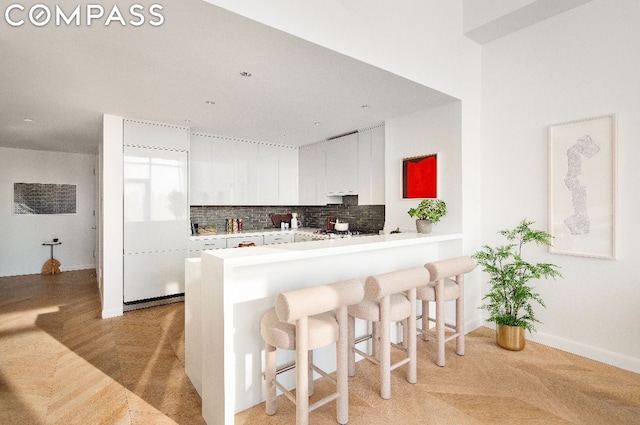 kitchen featuring a breakfast bar, white cabinetry, kitchen peninsula, decorative backsplash, and light parquet floors