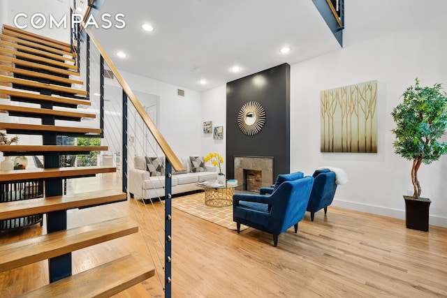 living area featuring stairs, a tile fireplace, recessed lighting, and wood finished floors