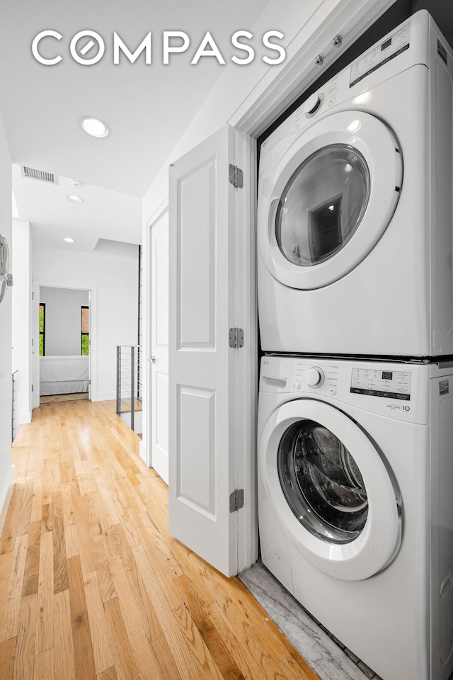 laundry area featuring stacked washer / drying machine, visible vents, light wood-style flooring, laundry area, and baseboards