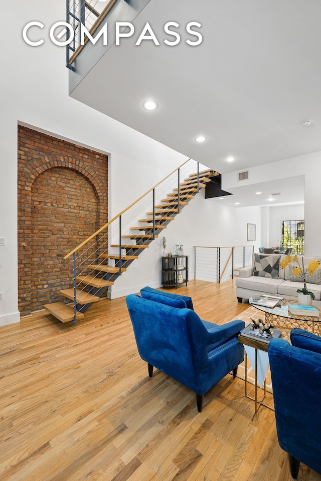 living area featuring brick wall, visible vents, stairway, and wood finished floors