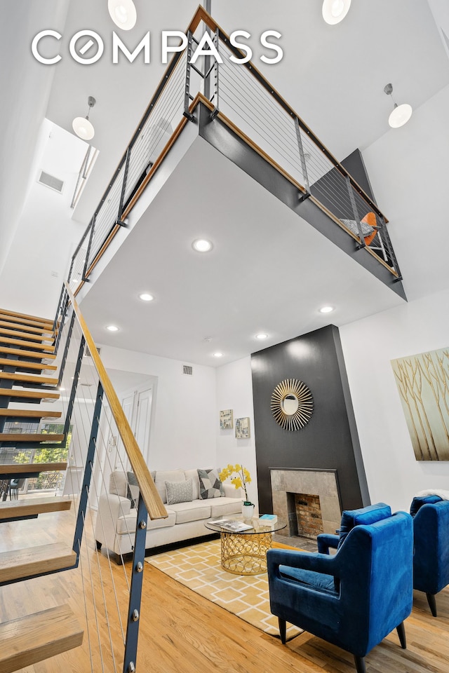 living room featuring a fireplace, visible vents, a towering ceiling, wood finished floors, and stairs