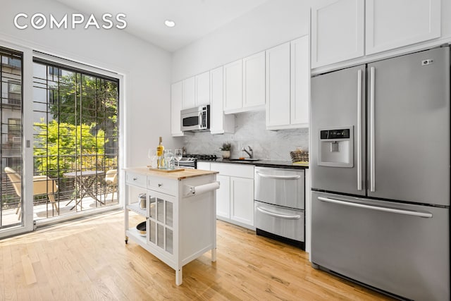 kitchen featuring light wood finished floors, butcher block counters, appliances with stainless steel finishes, a sink, and backsplash