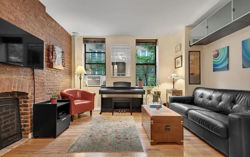 living area featuring cooling unit, a brick fireplace, light wood-style flooring, and brick wall