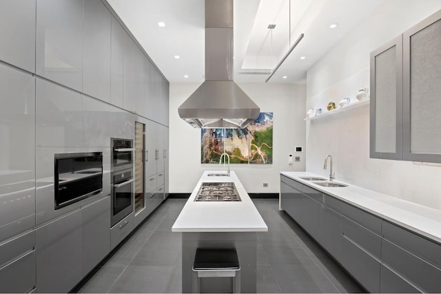 kitchen with sink, gray cabinetry, island range hood, and dark tile patterned floors