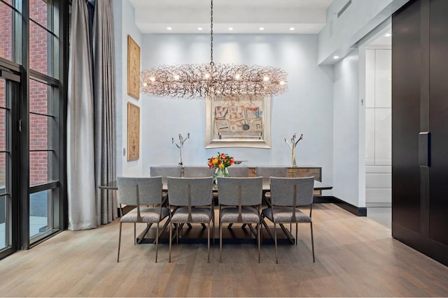 dining space with a high ceiling, a chandelier, and light hardwood / wood-style flooring