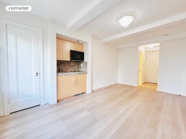 kitchen with beam ceiling, black microwave, light brown cabinetry, light wood-type flooring, and backsplash