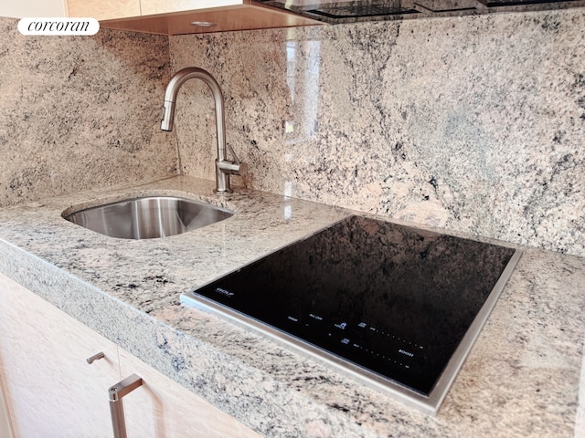 interior details featuring a sink, backsplash, black electric stovetop, and light stone countertops