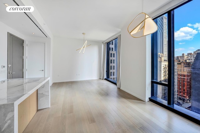 unfurnished dining area with light wood finished floors, a wall of windows, visible vents, and baseboards