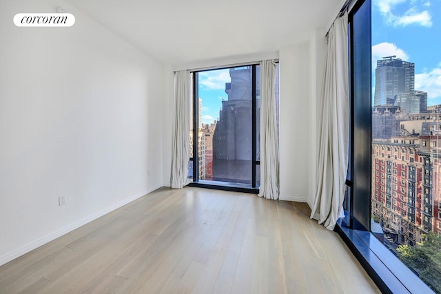 unfurnished room featuring a view of city, wood finished floors, visible vents, and baseboards