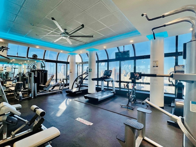 workout area featuring ceiling fan, a wall of windows, a raised ceiling, and a healthy amount of sunlight