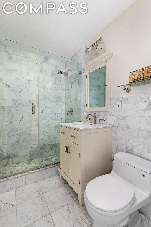 bathroom with toilet, tile walls, a shower with door, and vanity