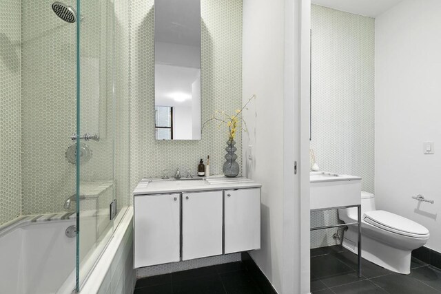 full bath featuring tile patterned flooring, vanity, toilet, and bath / shower combo with glass door