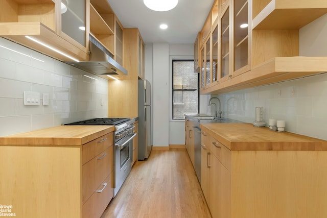 kitchen featuring wood counters, appliances with stainless steel finishes, a sink, light wood-type flooring, and backsplash