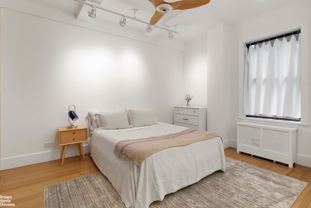 bedroom with ceiling fan, radiator heating unit, track lighting, and hardwood / wood-style floors