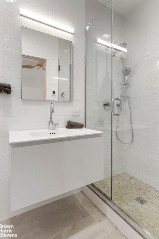 bathroom featuring decorative backsplash, tile walls, a shower with shower door, and vanity