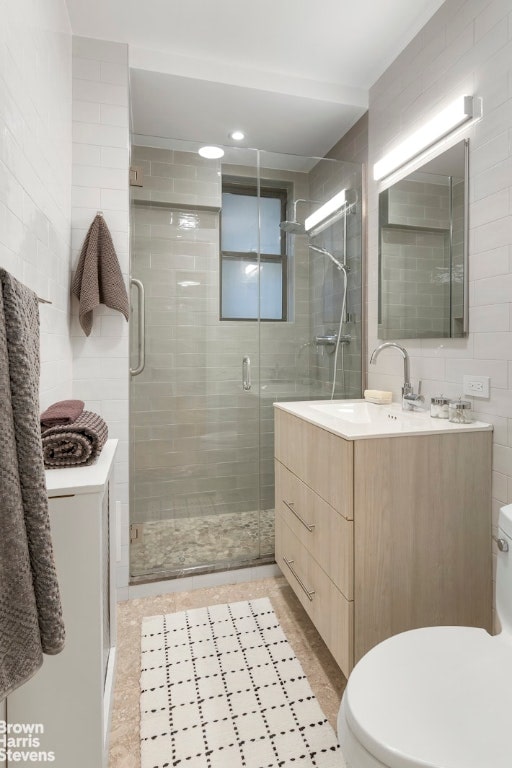 bathroom with toilet, vanity, tile walls, tile patterned flooring, and an enclosed shower