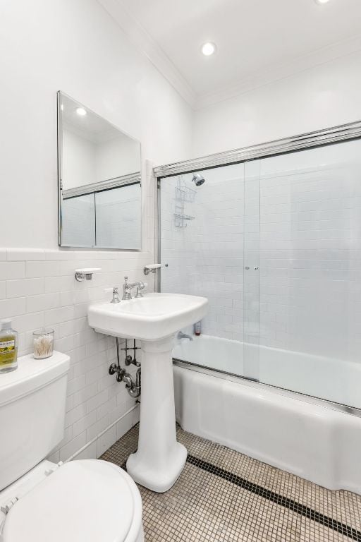 bathroom featuring tile patterned floors, toilet, crown molding, bath / shower combo with glass door, and tile walls