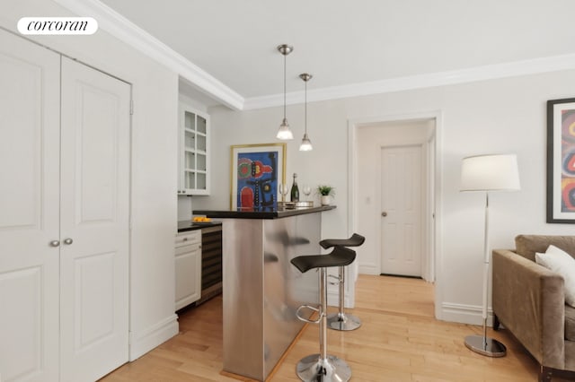 kitchen with a kitchen bar, crown molding, white cabinetry, hanging light fixtures, and light wood-type flooring