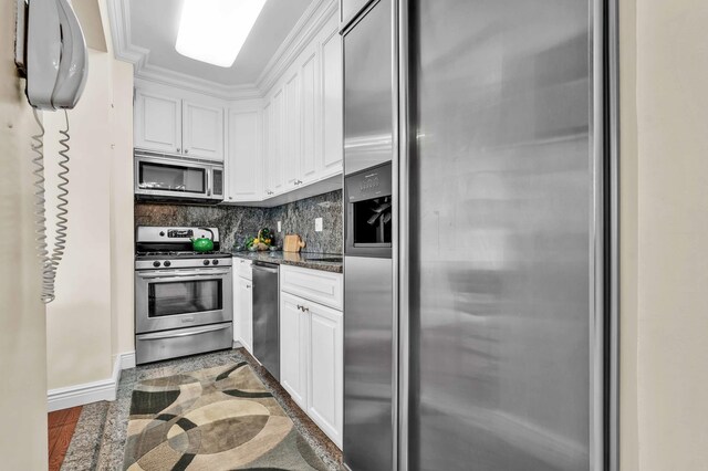 kitchen featuring appliances with stainless steel finishes, white cabinets, tasteful backsplash, dark stone counters, and baseboards