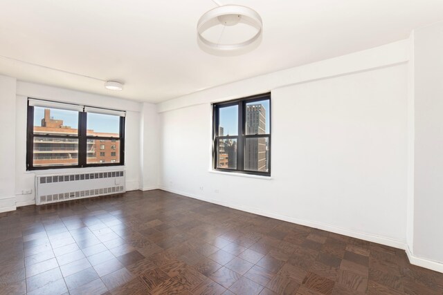 unfurnished room featuring baseboards, radiator heating unit, and plenty of natural light