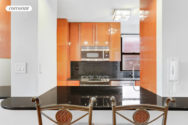 kitchen with sink, backsplash, stainless steel appliances, and dark stone countertops