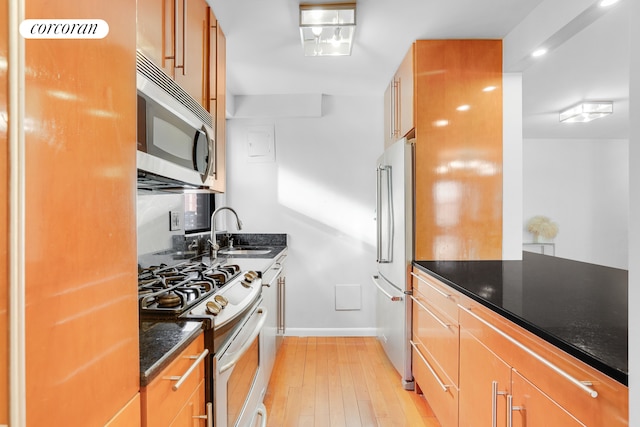 kitchen featuring light wood-style flooring, a sink, baseboards, appliances with stainless steel finishes, and dark stone countertops