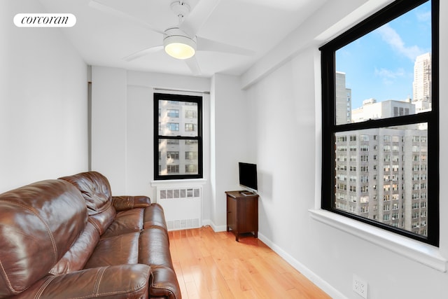 living area featuring ceiling fan, wood finished floors, visible vents, baseboards, and radiator heating unit