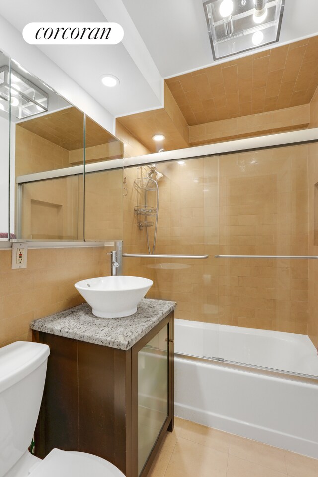 full bathroom with toilet, bath / shower combo with glass door, tile walls, tile patterned flooring, and vanity