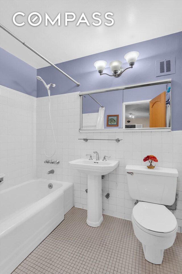 bathroom featuring tile patterned flooring, tub / shower combination, tile walls, and toilet