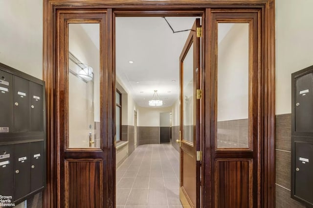 corridor with a mail area, light tile patterned floors, and tile walls