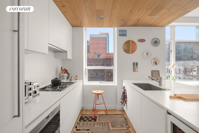 kitchen featuring a sink, white cabinets, stainless steel gas stovetop, beverage cooler, and wooden ceiling