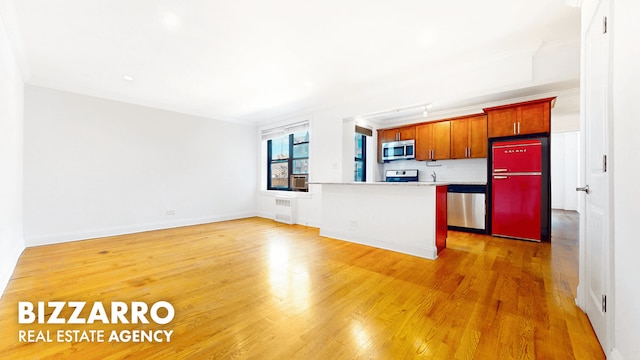 kitchen with appliances with stainless steel finishes, ornamental molding, radiator, light countertops, and light wood finished floors