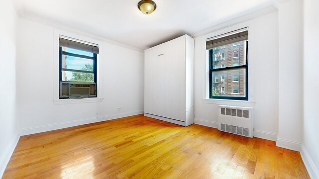 kitchen with crown molding, radiator heating unit, kitchen peninsula, and light hardwood / wood-style flooring