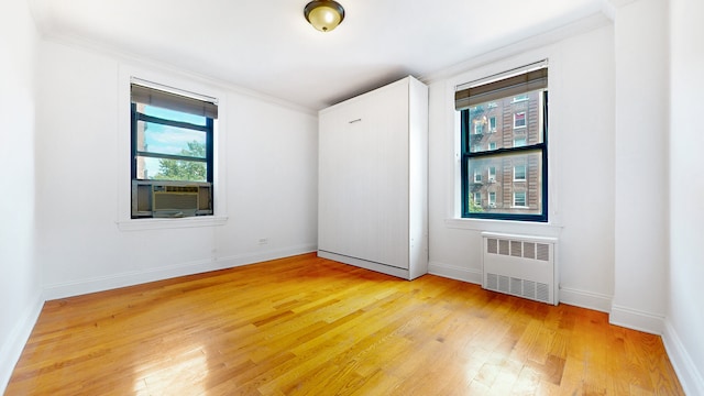 unfurnished room with radiator, light wood finished floors, cooling unit, baseboards, and ornamental molding
