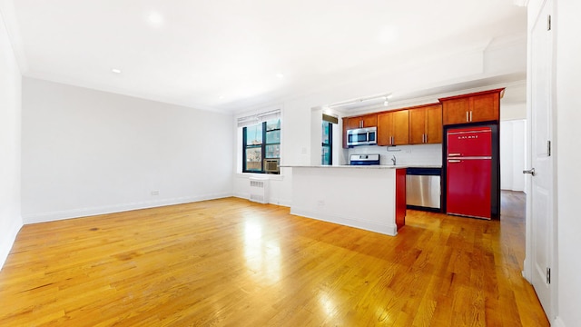 kitchen featuring ornamental molding, appliances with stainless steel finishes, light hardwood / wood-style flooring, and radiator heating unit