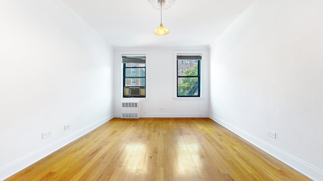 empty room with radiator, crown molding, light wood finished floors, and baseboards