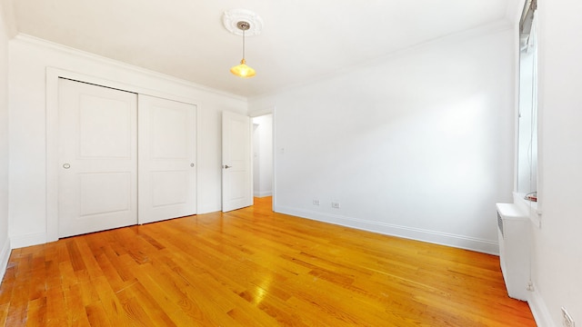 unfurnished bedroom with crown molding, light wood-style floors, baseboards, and a closet