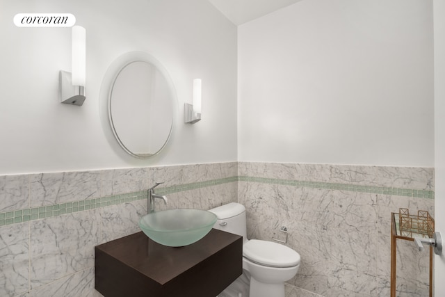 half bathroom with toilet, a wainscoted wall, tile walls, and vanity