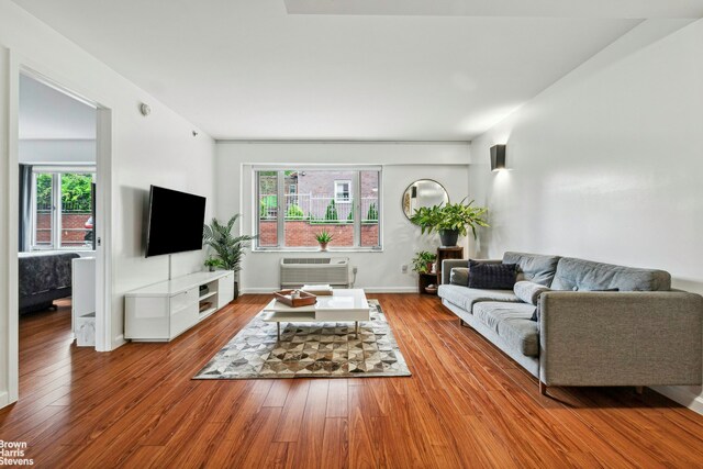 living room featuring wood-type flooring, a wall mounted air conditioner, and baseboards